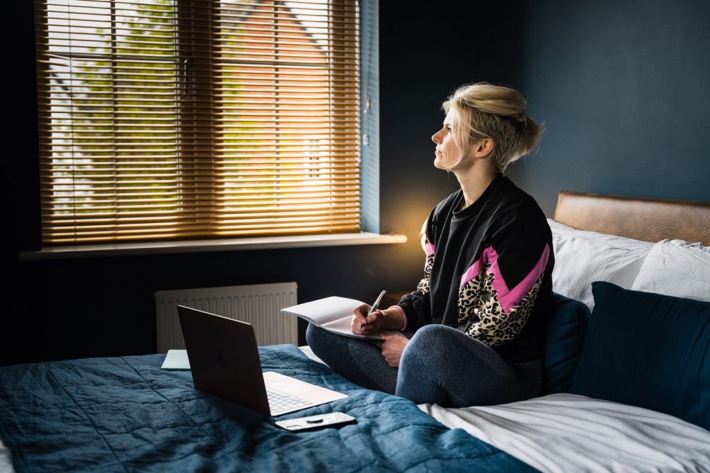 woman sat on bed with laptop writing down ideas for her blog