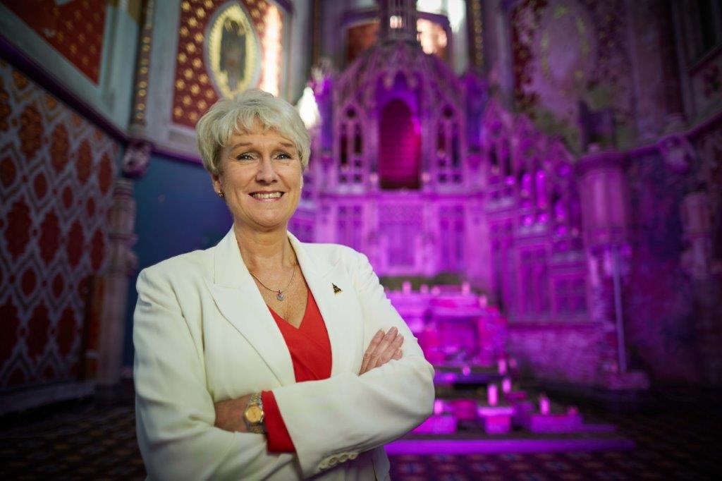 Elaine Griffiths OBE wearing a white jacket and standing in front of the high altar at The Monastery